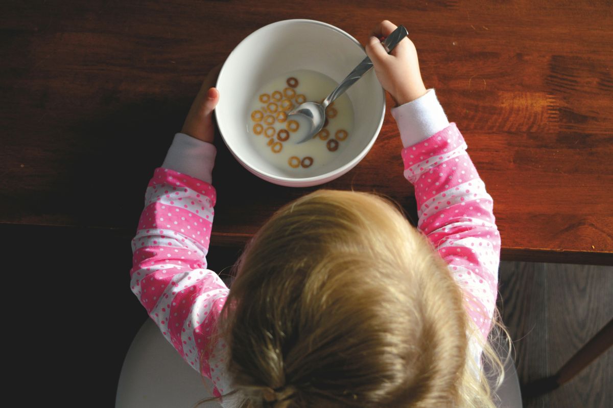Barn spiser frokostblanding fra en skål ved kjøkkenbordet