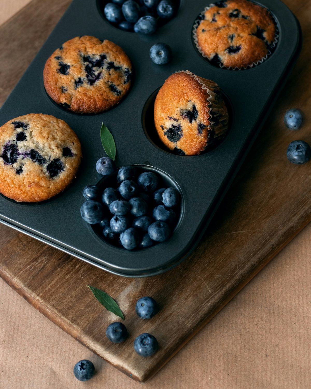 Blåbærmuffins i muffinsform på trefjøl med friske blåbær